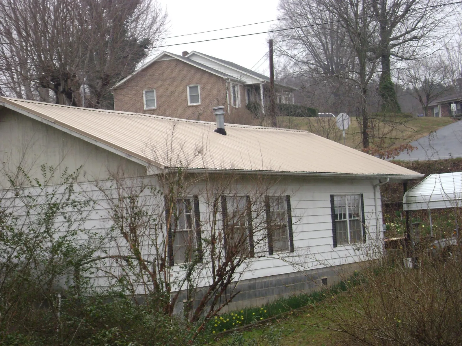 Tan metal roof on a white sided house set into a hillside — Commercial Roofing by Roofing Brothers in Riverton